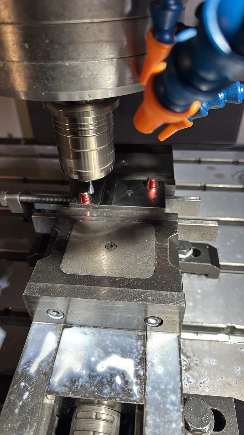 Eine Metallbearbeitungsmaschine fräst ein Werkstück, während Kühlmittel aus einer Düse gespritzt wird. Das Werkstück ist in einem Schraubstock befestigt.