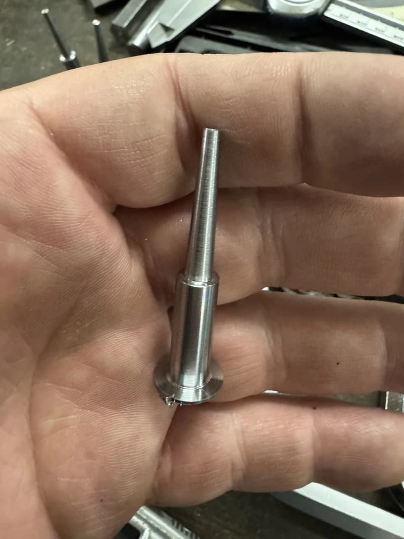 Nahaufnahme einer Hand, die einen kleinen, silberfarbenen Metallstift mit einem breiteren Sockel hält. Der Stift ist zylindrisch und verjüngt sich an der Spitze.